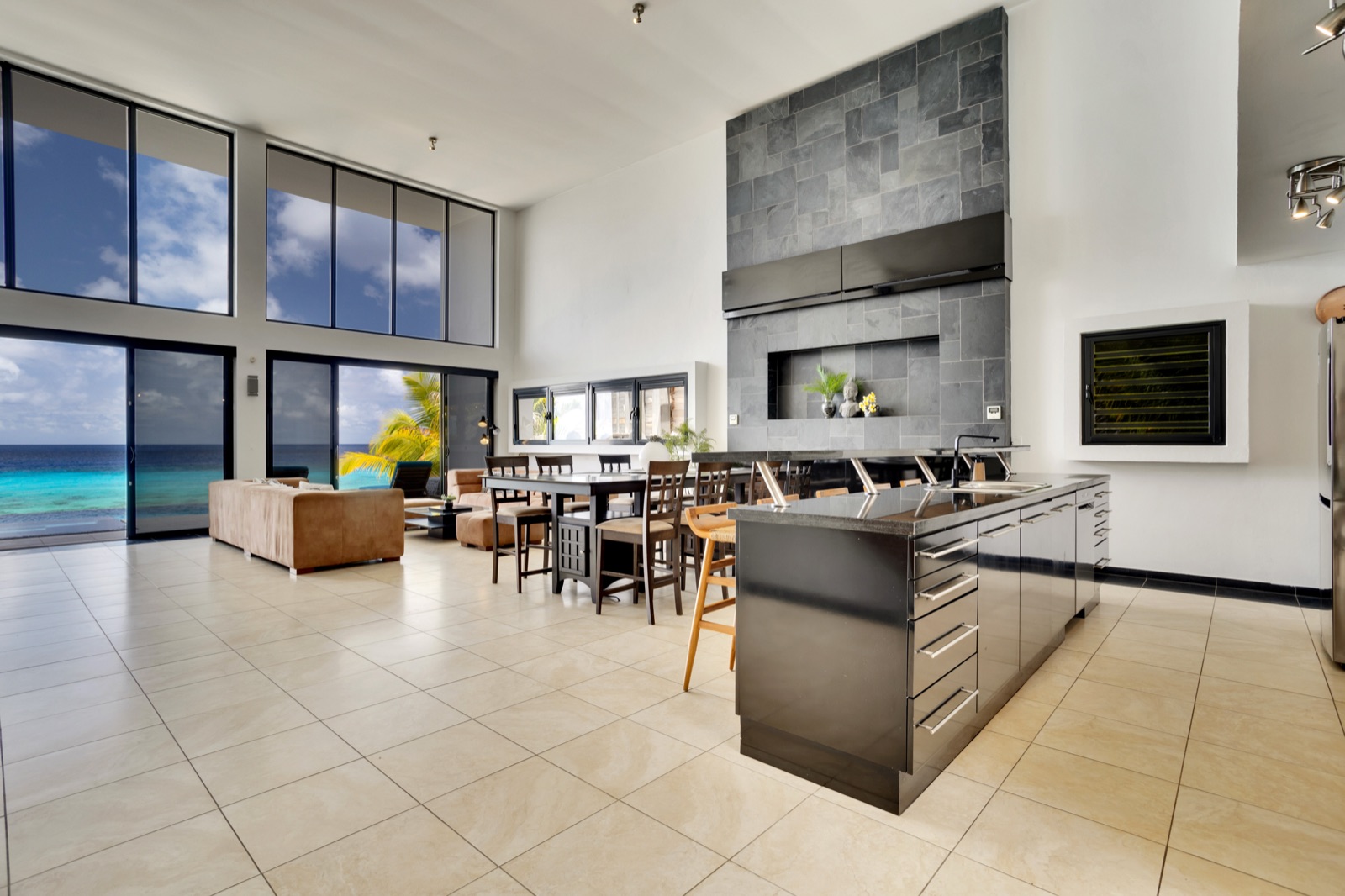 Luxury Bonaire villa's open-concept great room with a gourmet kitchen, double-height ceilings, and floor-to-ceiling windows framing the turquoise ocean.